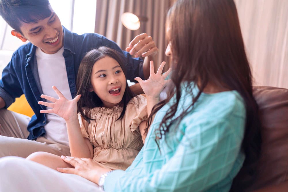 A child and two adults playing and laughing together indoors.