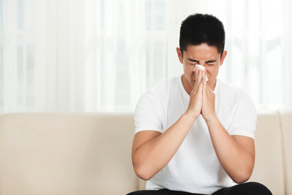 A woman experiencing nasal congestion or cold symptoms, sitting on a sofa at home.