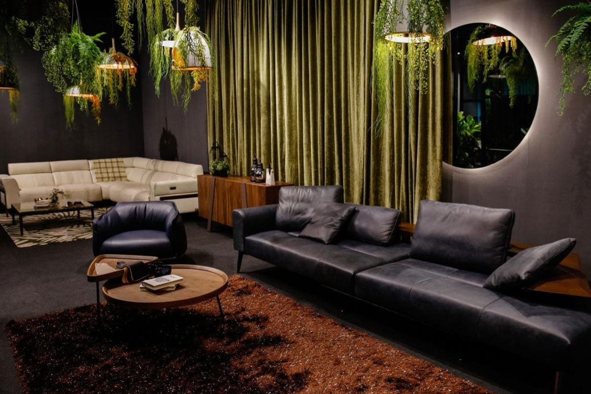 Modern stylish living room with black leather sofas, green curtains, and hanging plants.