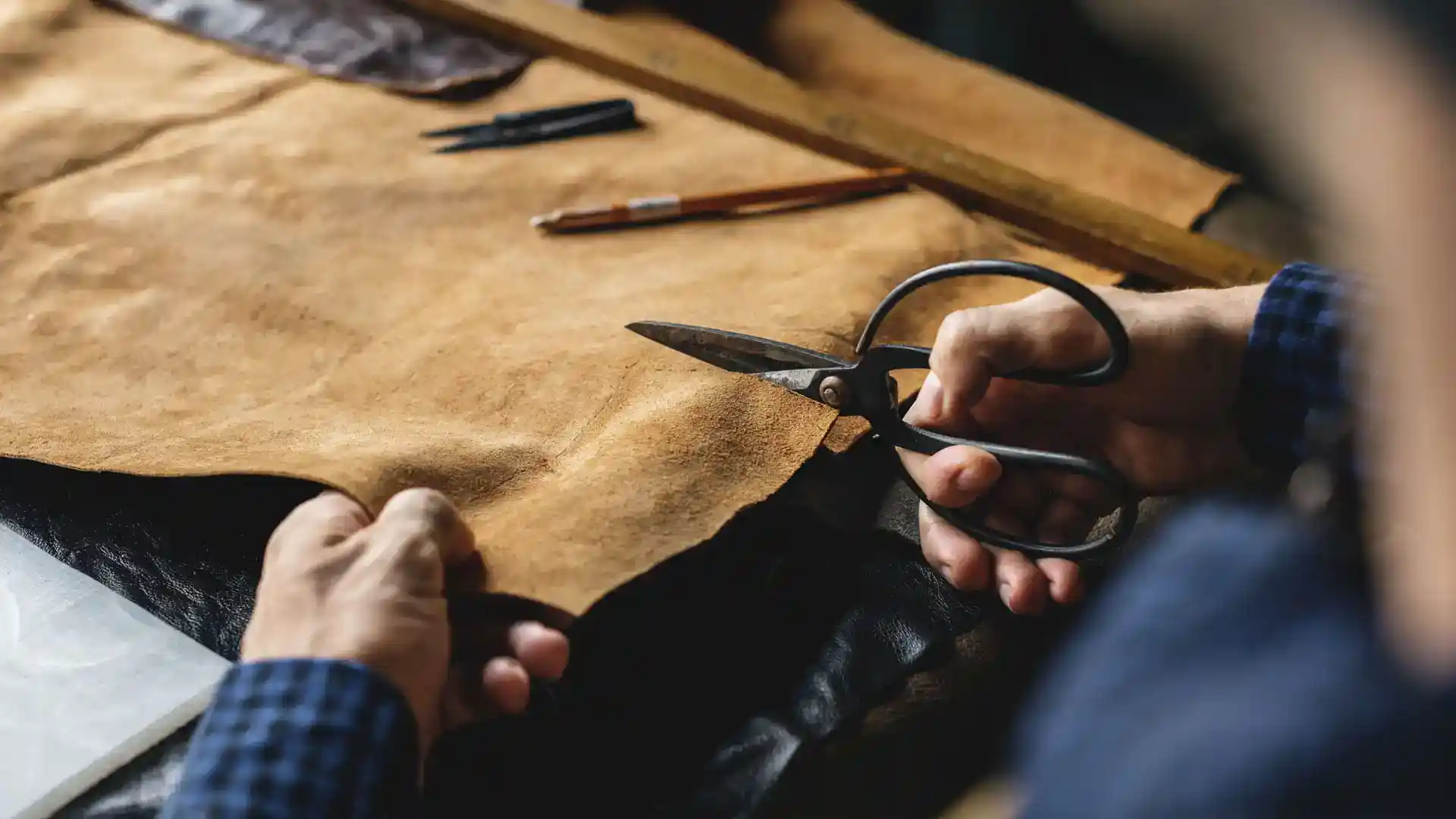 A professional craftsman cutting leather for custom product creation.