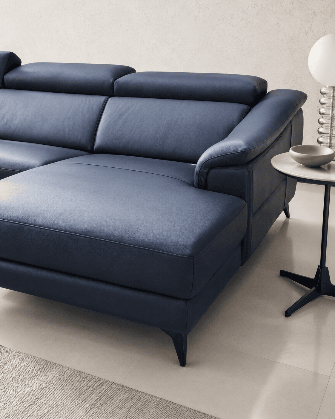 Modern blue leather sofa with black legs in a minimalist living room setting.